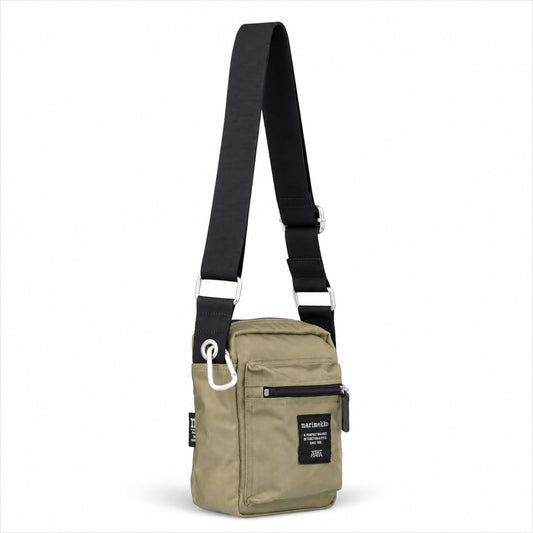 A small crossbody bag in olive green with a wide black adjustable strap, silver metal hardware, and a black brand patch on the front pocket, shown against a plain white background.