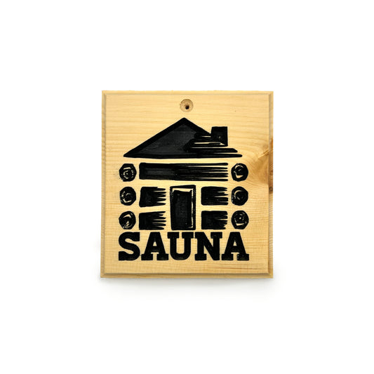 A square wooden sauna plaque or sign with a black engraved graphic of a log cabin and the word 'SAUNA' in bold letters, shown on a plain white background.