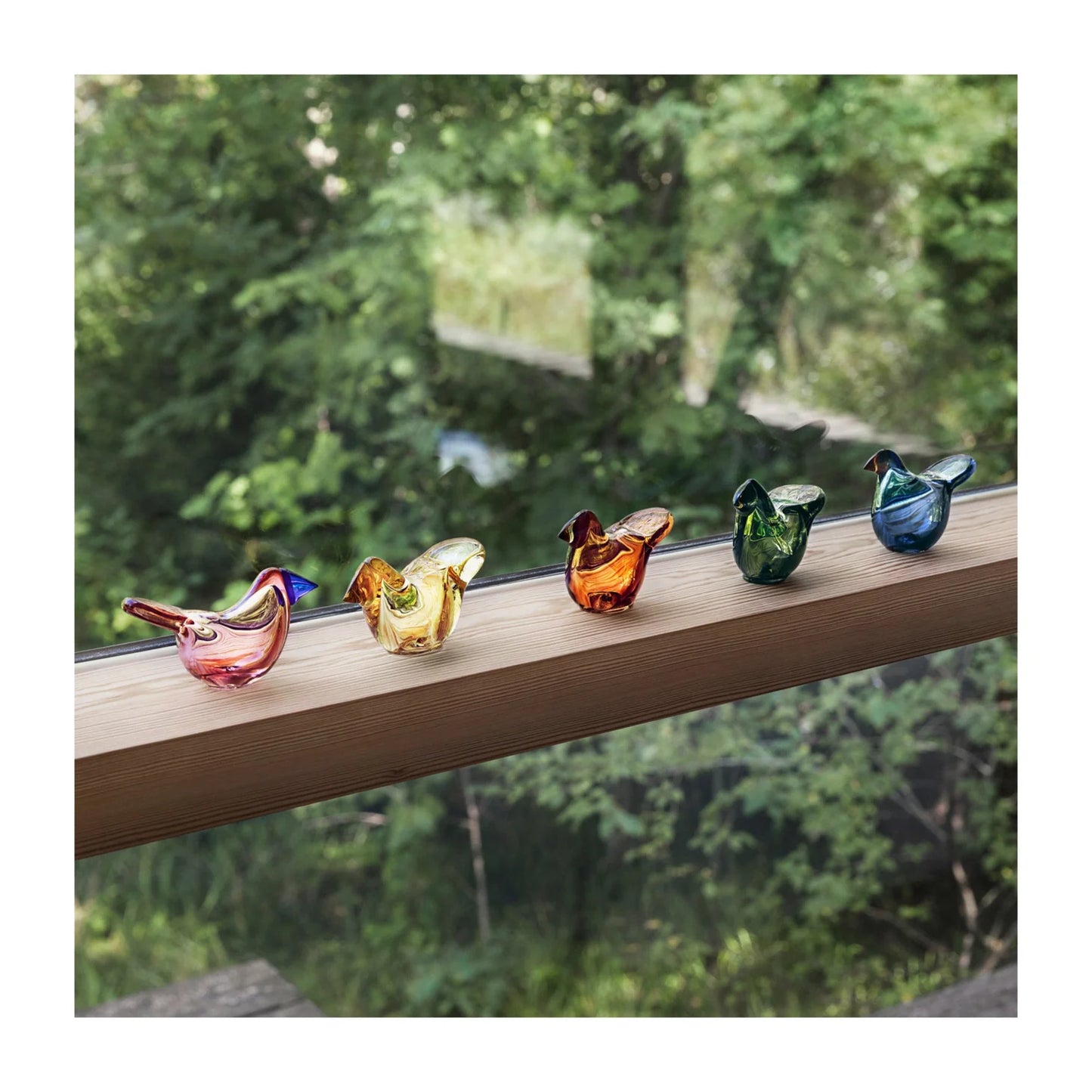 Colorful glass bird figurines on a wooden ledge with a natural background